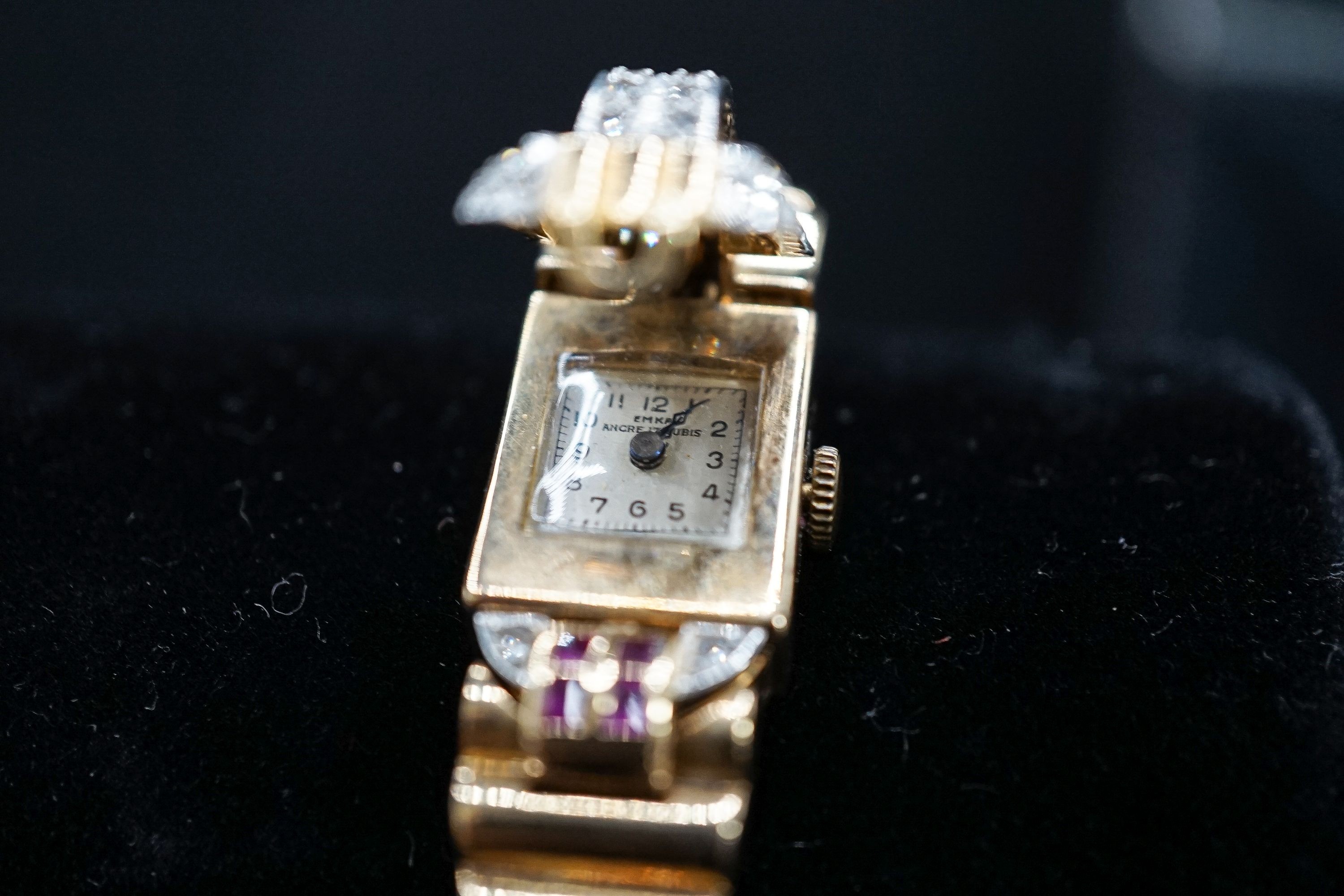 A 1950's 9ct gold, ruby and diamond set Emka manual wind cocktail watch, the dial with gem set hinged cover, gross weight 37.2 grams.